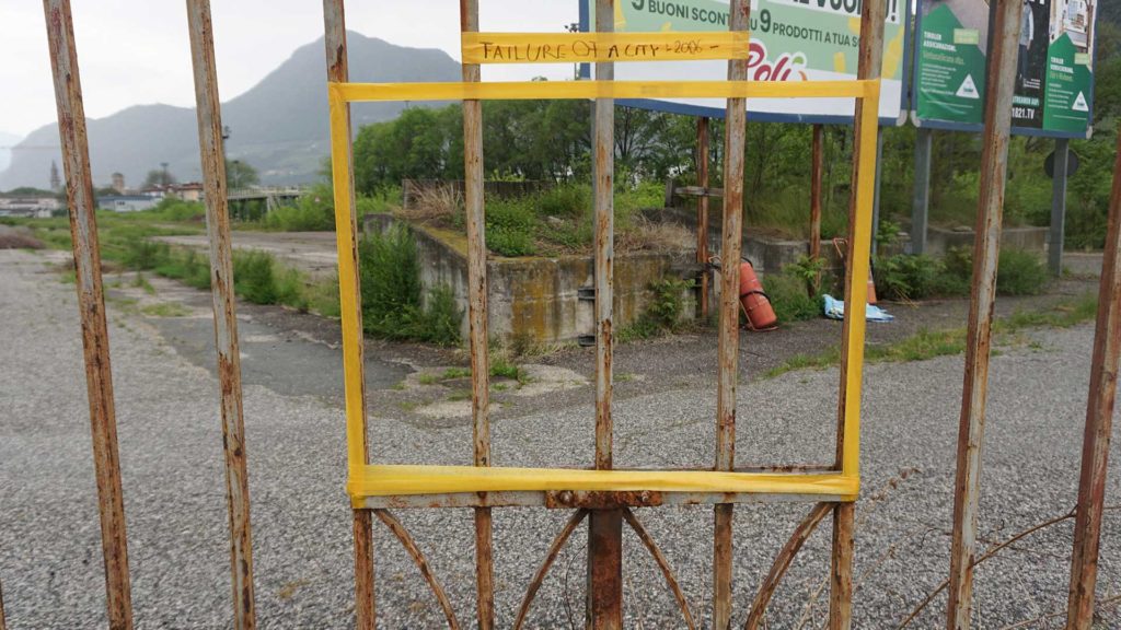 picture of a single orange frame taped onto the gate of the area on it there is written "failure of a city - 2006"