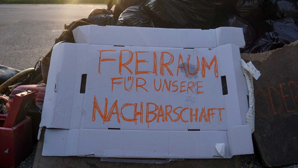 "Freiraum für unsere Nachbarschaft" written on a piece of cardboard in front of the trash mountain