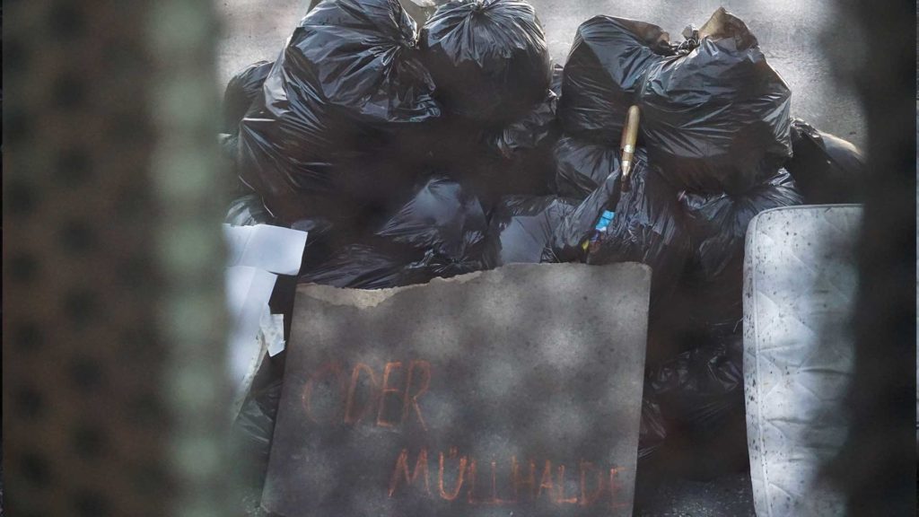 "oder Müllhalde" written on a piece of cardboard in front of the trash mountain